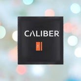 A black packet labeled "Caliber XL" features "CALIBER" in white and "XL" in orange, set against a background of soft, blurred colorful bokeh lights.